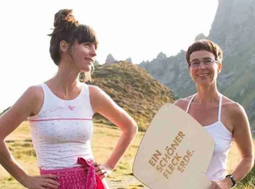 Zwei Frauen in Unterwäsche von Ein schöner Fleck Erde in den Alpen – nachhaltige Damenunterwäsche mit Bergmotiv, präsentiert mit Markenschild im Sonnenschein.