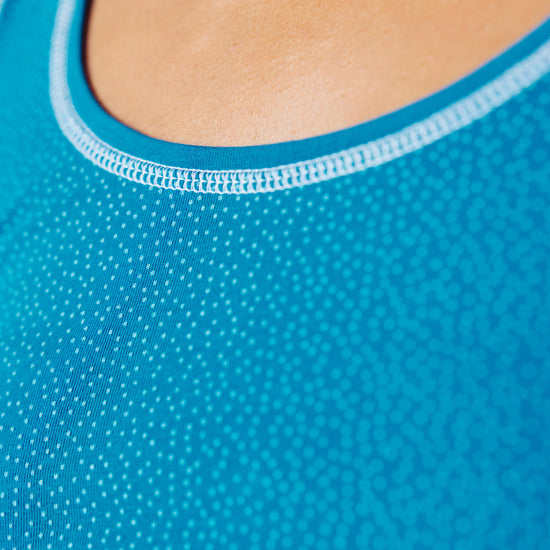 Detailansicht des Halsausschnitts eines blauen Tops mit feinem Punktmuster und hellblauer Einfassung; Fokus auf Stoffstruktur und Naht.