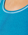 Detailansicht des Halsausschnitts eines blauen Tops mit feinem Punktmuster und hellblauer Einfassung; Fokus auf Stoffstruktur und Naht.