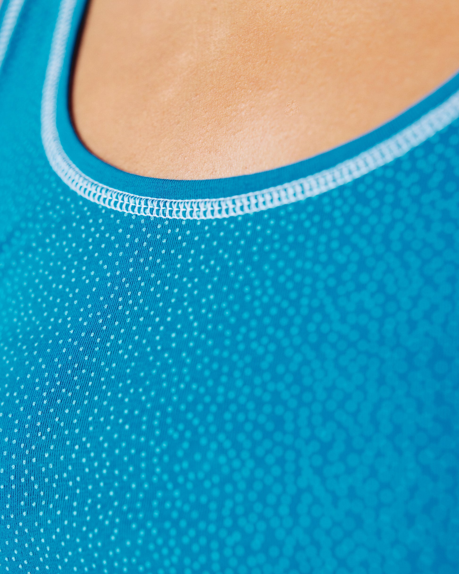 Detailansicht des Halsausschnitts eines blauen Tops mit feinem Punktmuster und hellblauer Einfassung; Fokus auf Stoffstruktur und Naht.