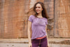 Frau trägt lilafarbenes T-Shirt mit Aufdruck Wald knallt und violette Funktionsleggings mit rotem Bund von Ein schöner Fleck Erde, Outdooraufnahme vor Felswand
