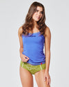 Frau in blauem Trägertop mit „Geheim“-Aufdruck und grünem Slip mit der Aufschrift „Hochwildstelle“, stehend vor neutralem, hellem Hintergrund.