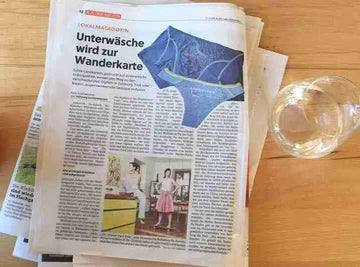 Zeitungsartikel über Ein schöner Fleck Erde mit Überschrift ‚Unterwäsche wird zur Wanderkarte‘ – Bericht über nachhaltige Damenunterwäsche mit alpinem Kartenmotiv.