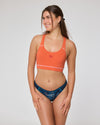 Lächelnde Frau in orangefarbenem Sport-BH und dunkelblauem Slip mit topografischem Kartendesign. Auf dem Slip steht der Schriftzug „Glöcknerin“.