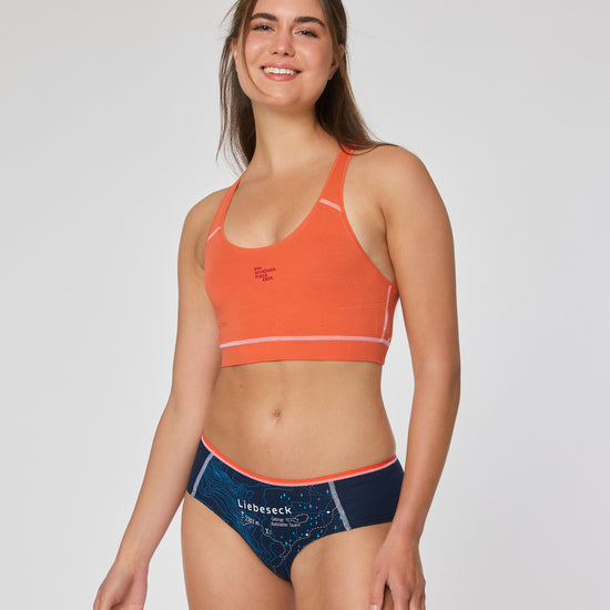 Frau in orangefarbenem Sport-Bustier und dunkelblauer Hipster Unterhose mit Aufdruck ‚Liebeseck