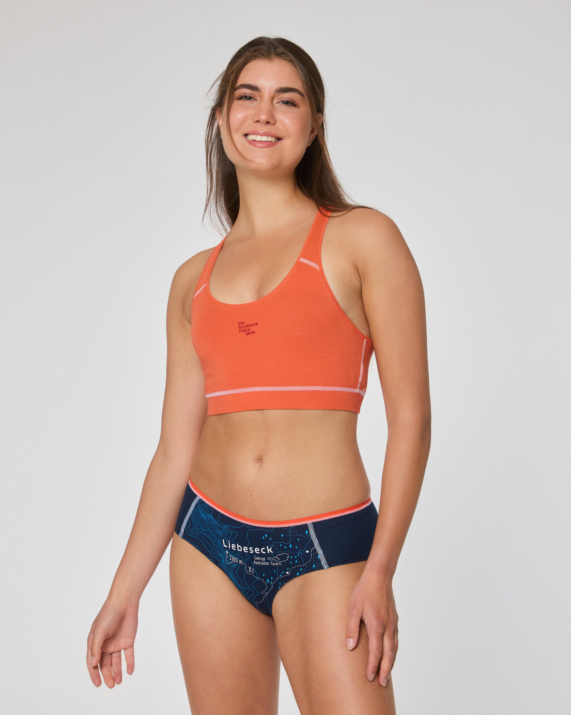 Frau in orangefarbenem Sport-Bustier und dunkelblauer Hipster Unterhose mit Aufdruck ‚Liebeseck