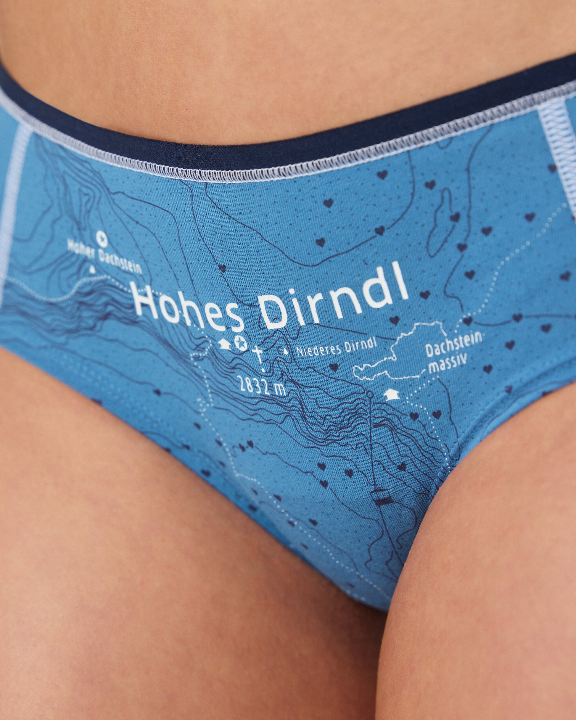 Detailaufnahme einer blauen Damen-Hipster-Unterhose mit topografischem Kartendruck. Im Zentrum steht die Beschriftung „Hohes Dirndl“ mit umliegenden geografischen Angaben wie „Hoher Dachstein“ und „Dachsteinmassiv“.