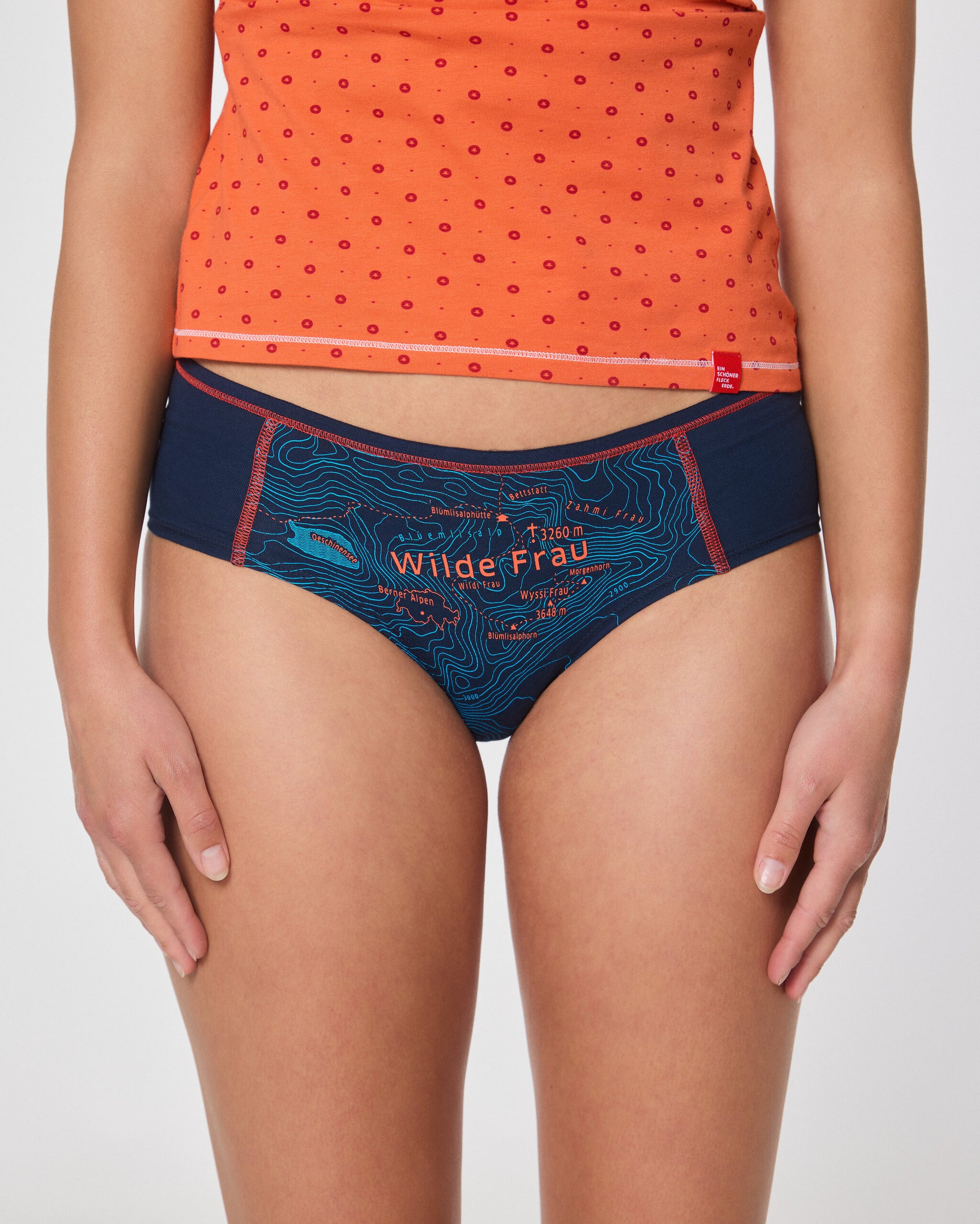 Frau in orangefarbenem Top und dunkelblauer Hipster Unterhose mit Aufdruck ‚Wilde Frau