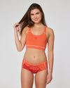 Frau trägt oranges Bustier und orangen Panty-Slip mit Aufdruck ‚Hexe‘ von Ein schöner Fleck Erde