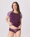 Frau trägt violett-lilafarbenes T-Shirt mit gelben Linien und passende Unterhose mit Aufdruck LUST AU von Ein schöner Fleck Erde, Studioaufnahme