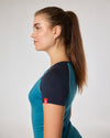 Seitenansicht einer Frau im zweifarbigen Kurzarmshirt in Blau und Petrol mit kleinem roten Label am Ärmel.