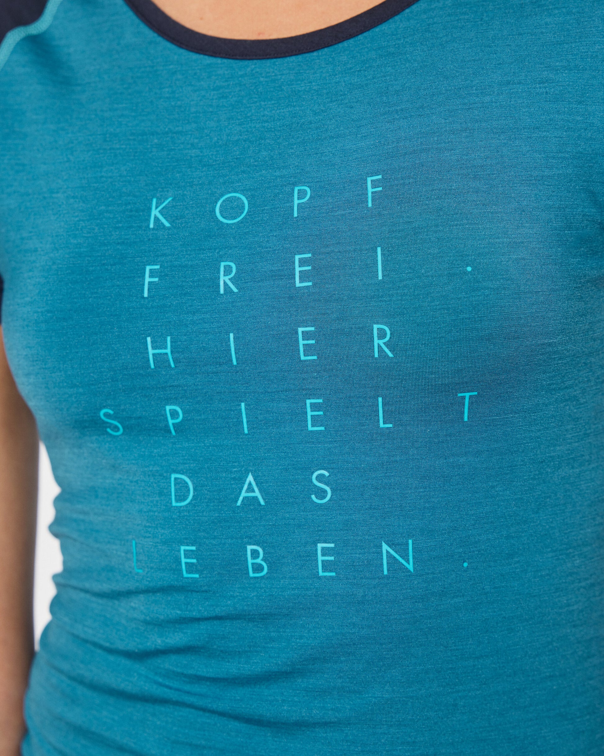 Nahaufnahme eines blauen T-Shirts mit türkisfarbenem Aufdruck ‚Kopf frei – hier spielt das Leben‘.