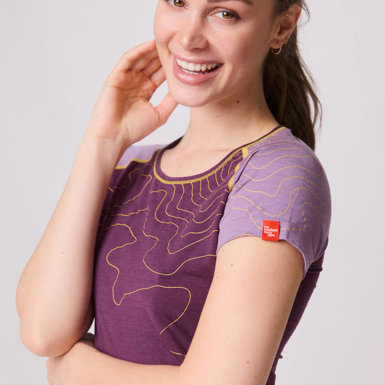Frau lächelt in Nahaufnahme und trägt violettes Funktionsshirt mit gelben Linien und kurzem Ärmel von Ein schöner Fleck Erde, Studioaufnahme