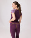 Rückansicht einer Frau in violettem Funktionsshirt und passender ¾-Leggings mit gelben Nähten von Ein schöner Fleck Erde, Studioaufnahme