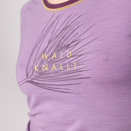 Detailaufnahme eines lilafarbenen T-Shirts mit gelbem Schriftzug Wald knallt und Kiefernmotiv von Ein schöner Fleck Erde