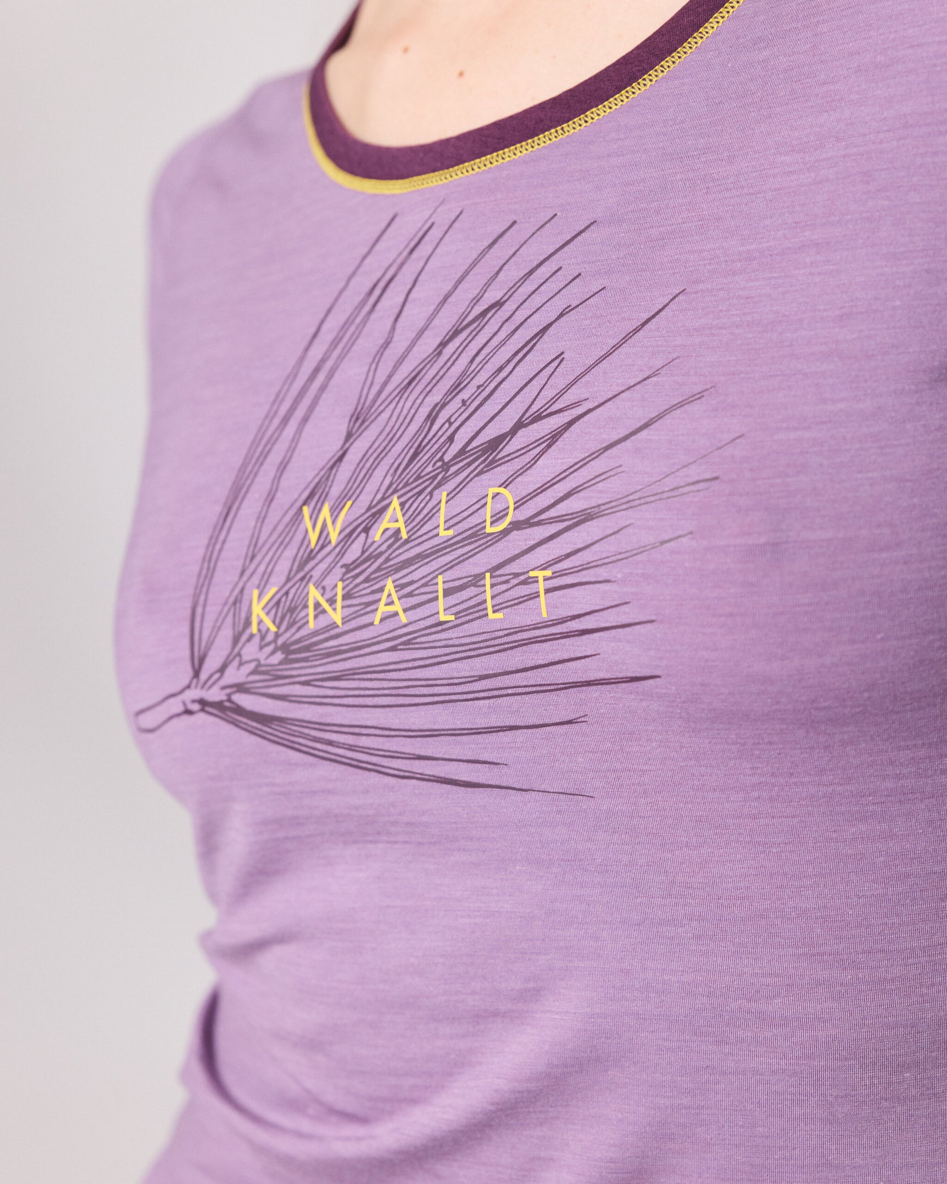 Detailaufnahme eines lilafarbenen T-Shirts mit gelbem Schriftzug Wald knallt und Kiefernmotiv von Ein schöner Fleck Erde