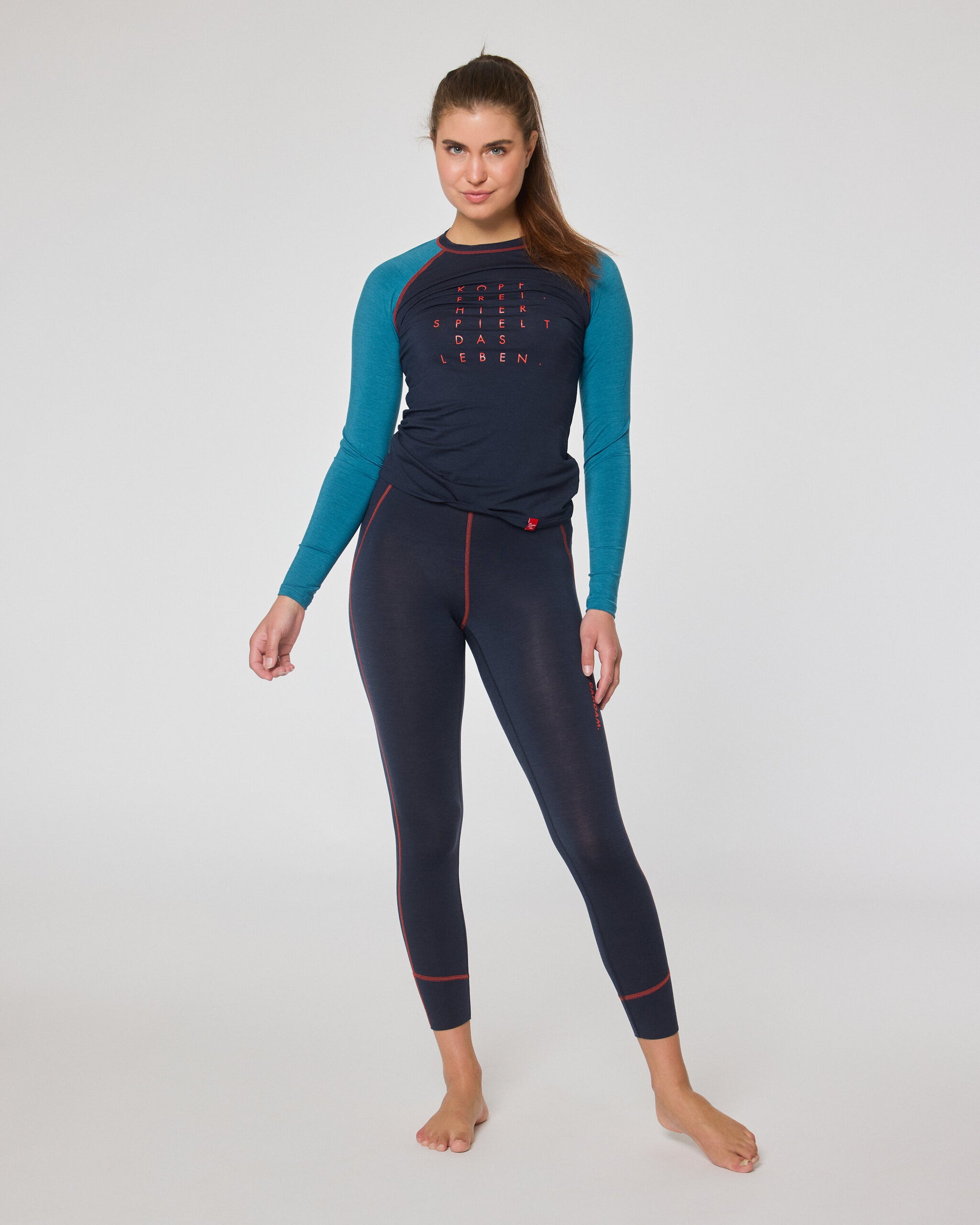Frau trägt ein dunkelblaues Longsleeve mit türkisfarbenen Ärmeln und rotem Schriftzug sowie eine dunkelblaue Leggings mit roten Nähten.