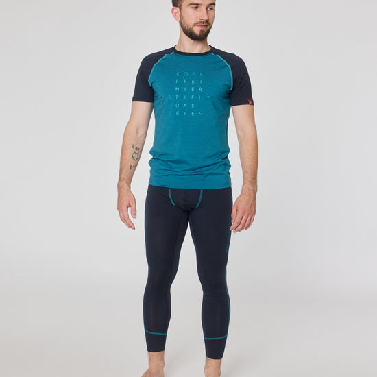 Mann trägt dunkelblaue Funktionsleggings und türkisfarbenes Kurzarmshirt von Ein schöner Fleck Erde, stehend vor neutralem Hintergrund