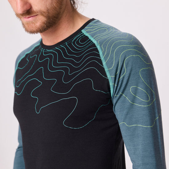 Detailaufnahme eines dunkelblauen Funktionsshirts mit hellblauen Ärmeln und Linienmuster von Ein schöner Fleck Erde, getragen von einem Mann im Studio