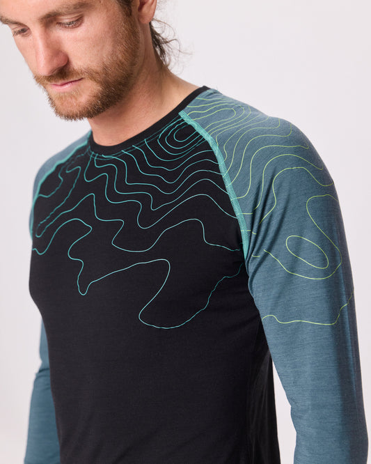 Detailaufnahme eines dunkelblauen Funktionsshirts mit hellblauen Ärmeln und Linienmuster von Ein schöner Fleck Erde, getragen von einem Mann im Studio
