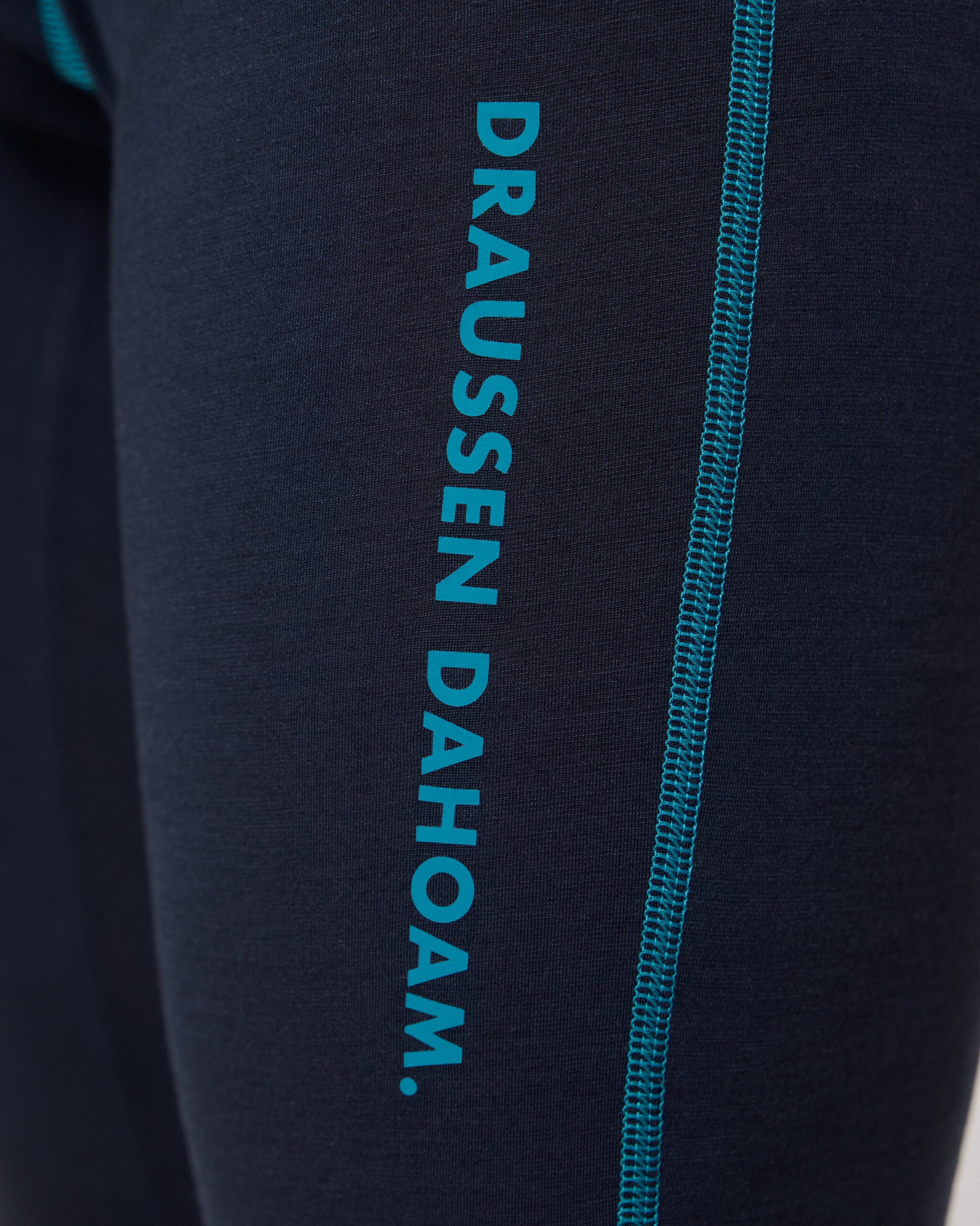 Detailaufnahme einer dunkelblauen Funktionsleggings mit türkisfarbener Naht und seitlichem Aufdruck ‚DRAUSSEN DAHOAM‘ von Ein schöner Fleck Erde.
